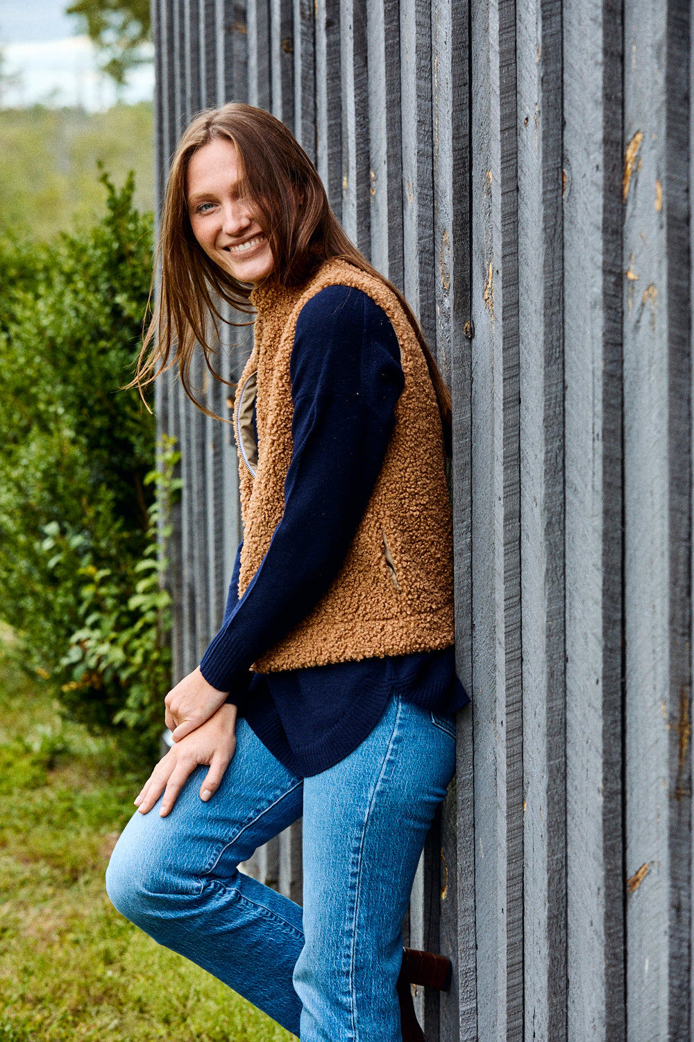 Woman wearing navy sweater, brown vest, and jeans.