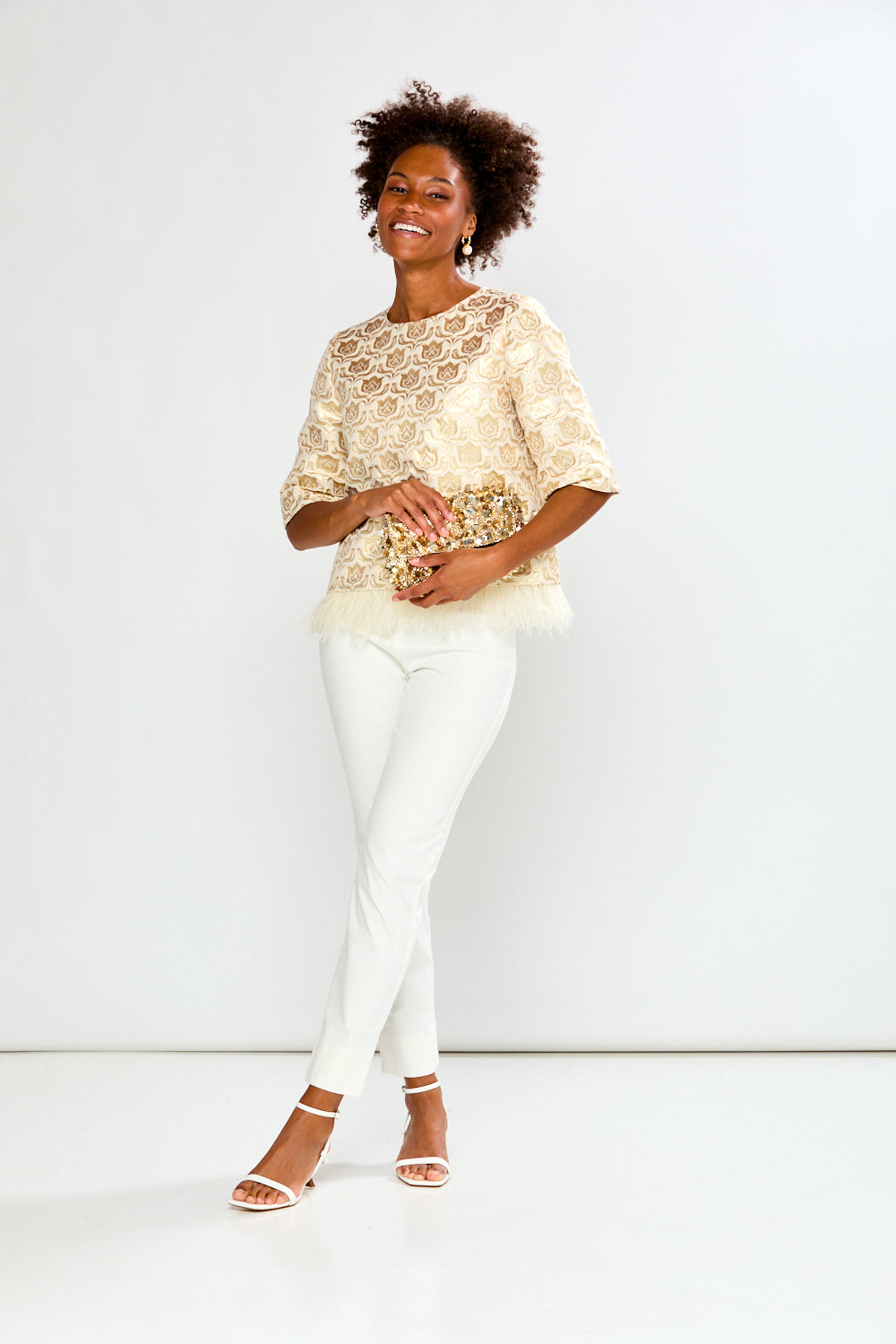 Woman wearing a beige lace top and white pants against a white background