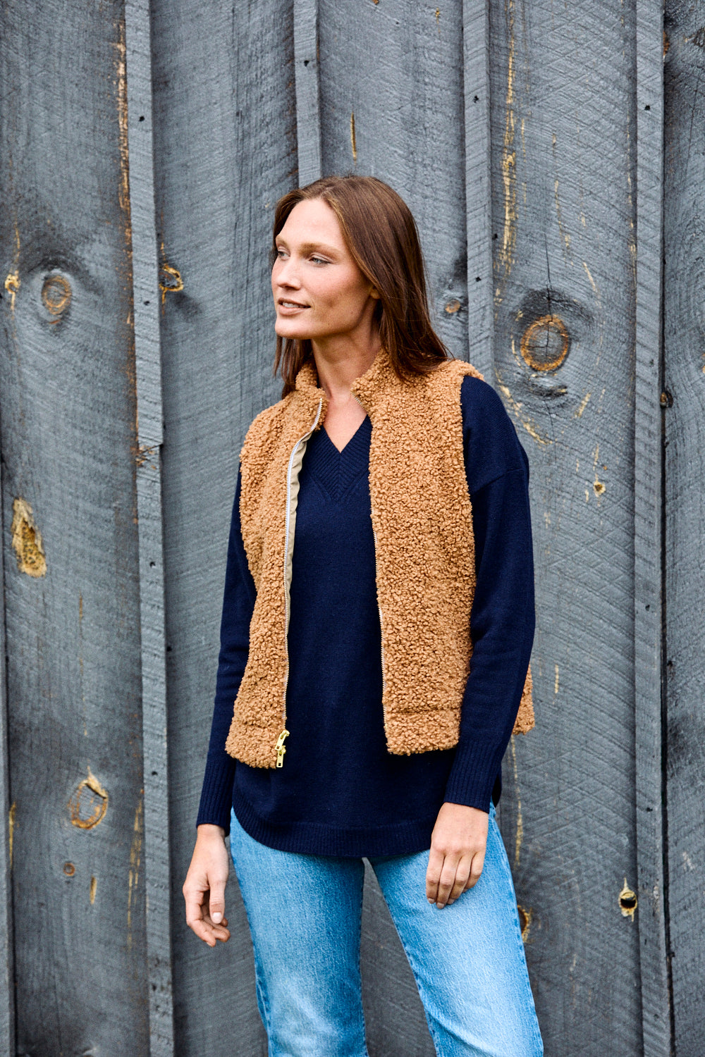Woman wearing navy sweater, brown vest, and jeans.