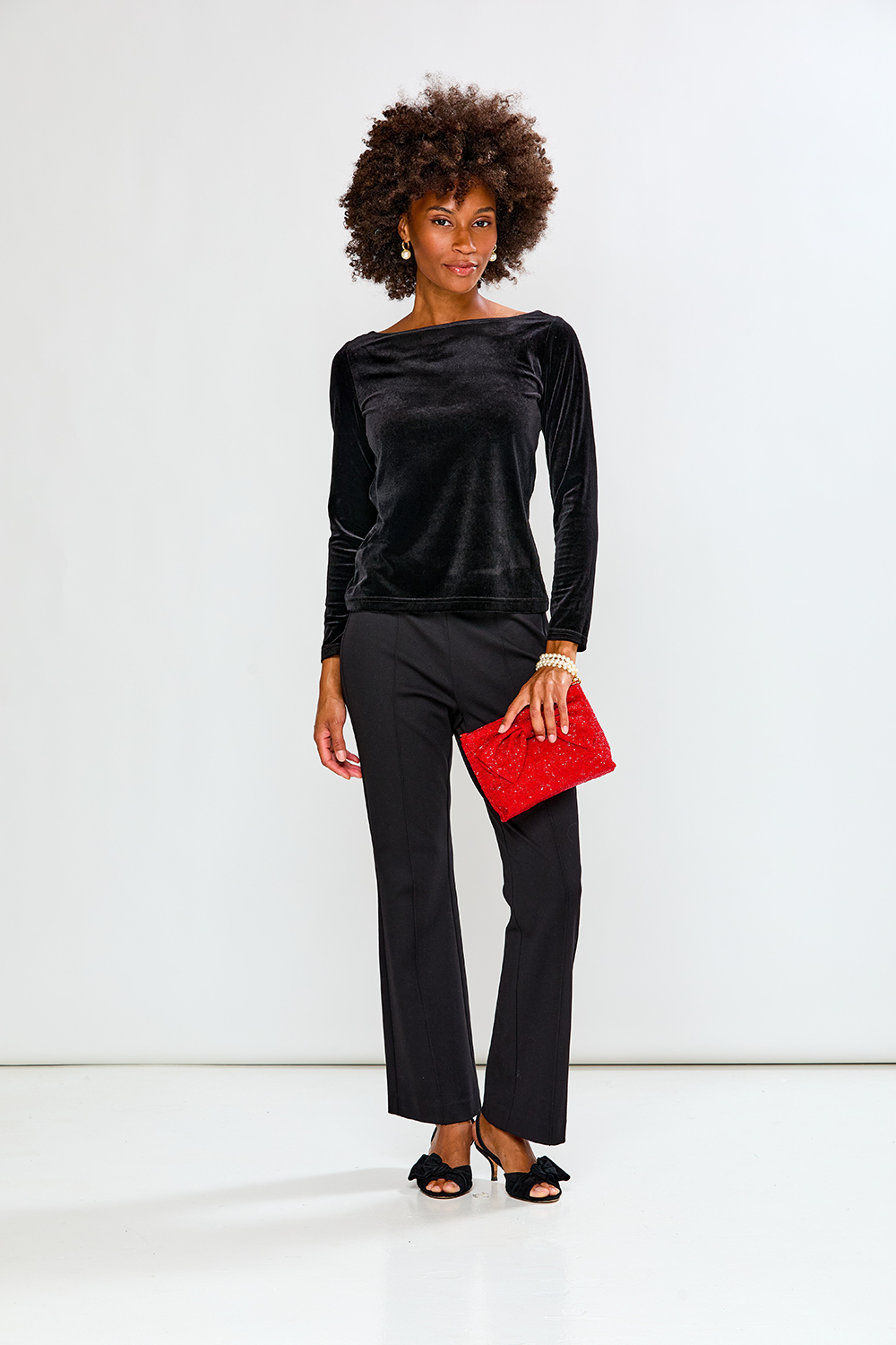 Woman in black outfit holding a red clutch against a white background