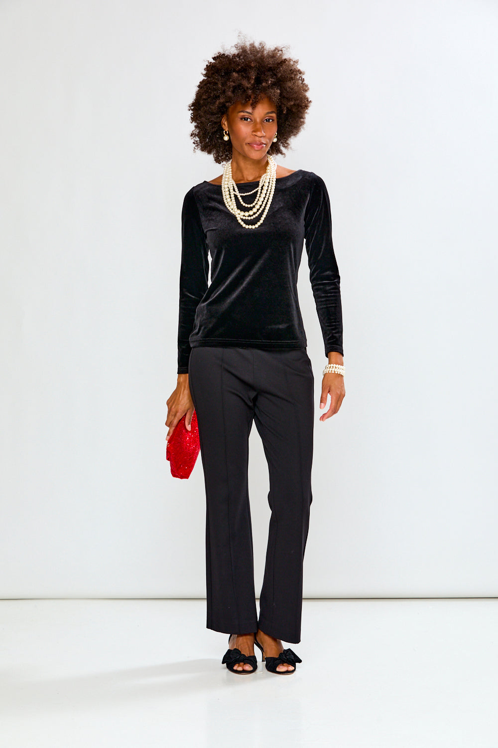 Woman wearing a black outfit with a red clutch against a white background