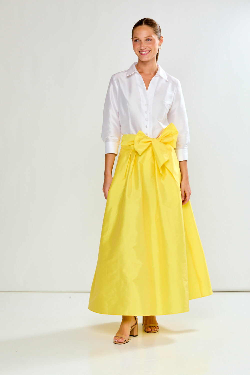 Woman wearing a white shirt and yellow skirt with a bow on a white background