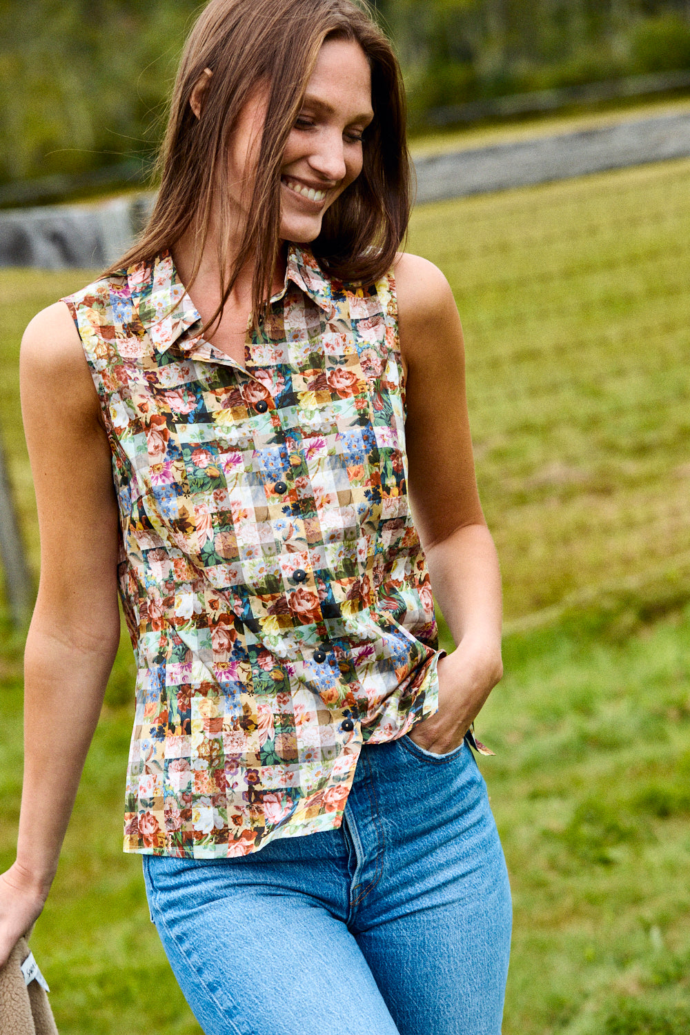 Woman wearing a colorful patterned sleeveless shirt and blue jeans outdoors.