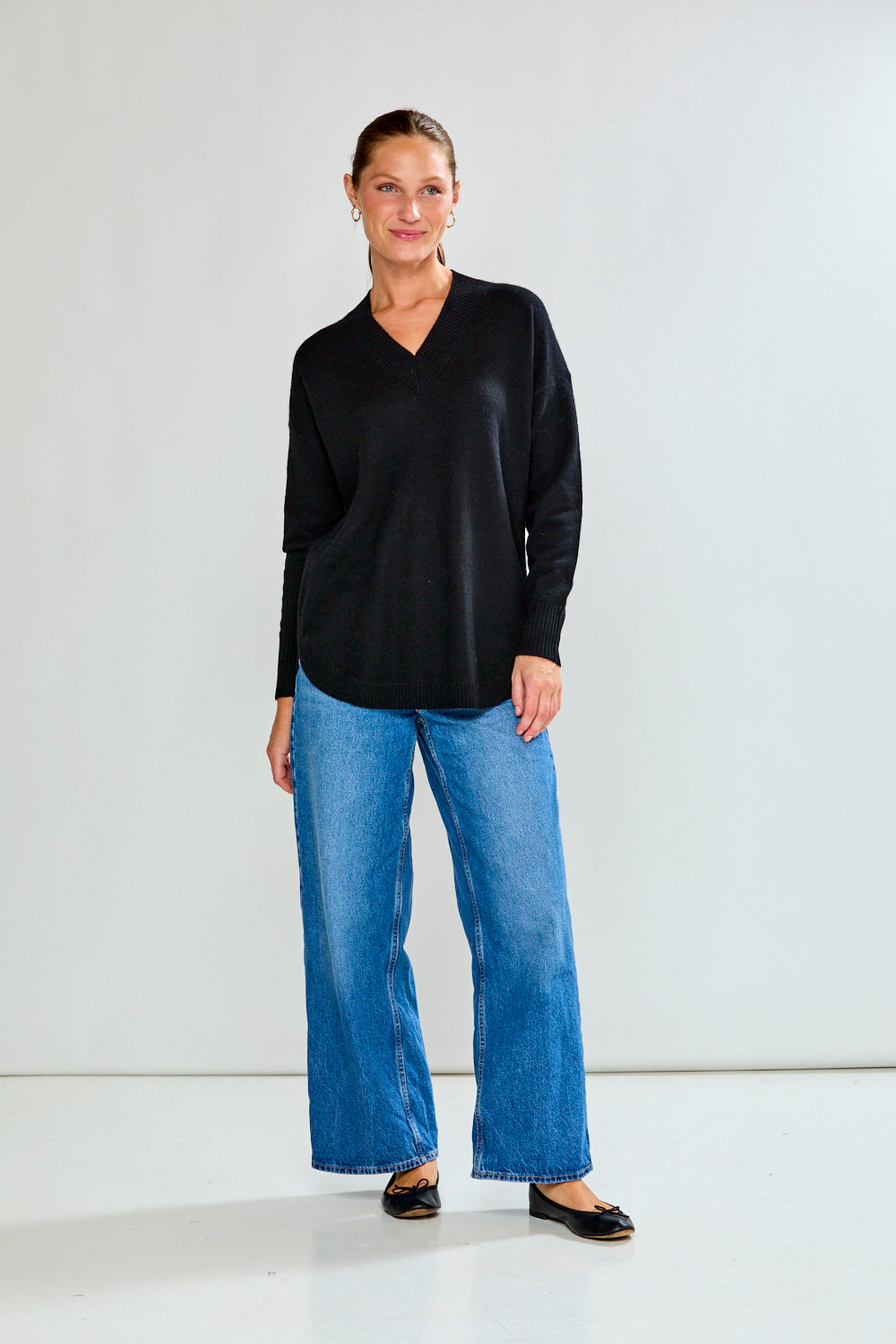 Woman wearing a black sweater and blue jeans against a plain background