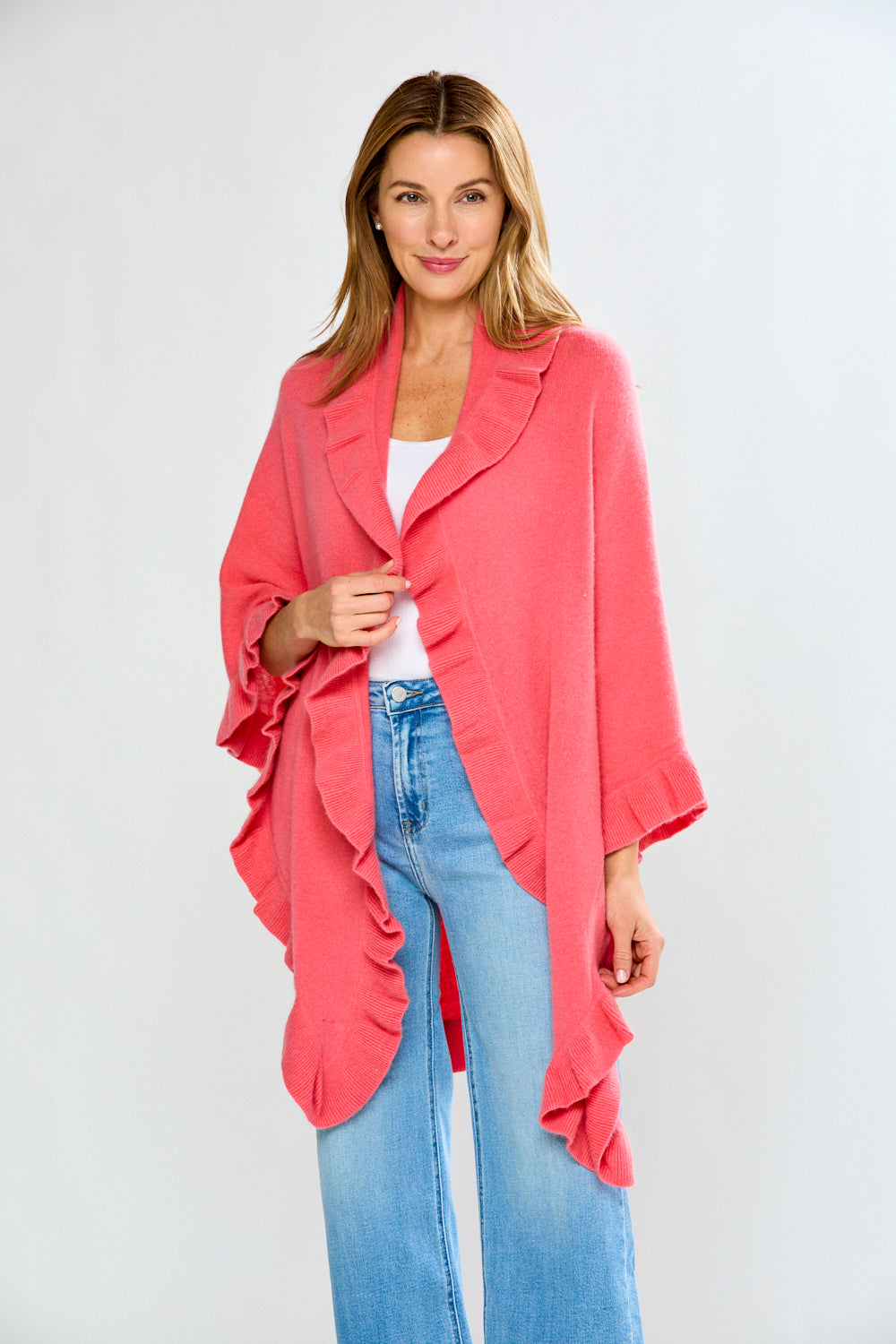 Woman wearing a pink cardigan over a white top and blue jeans on a white background