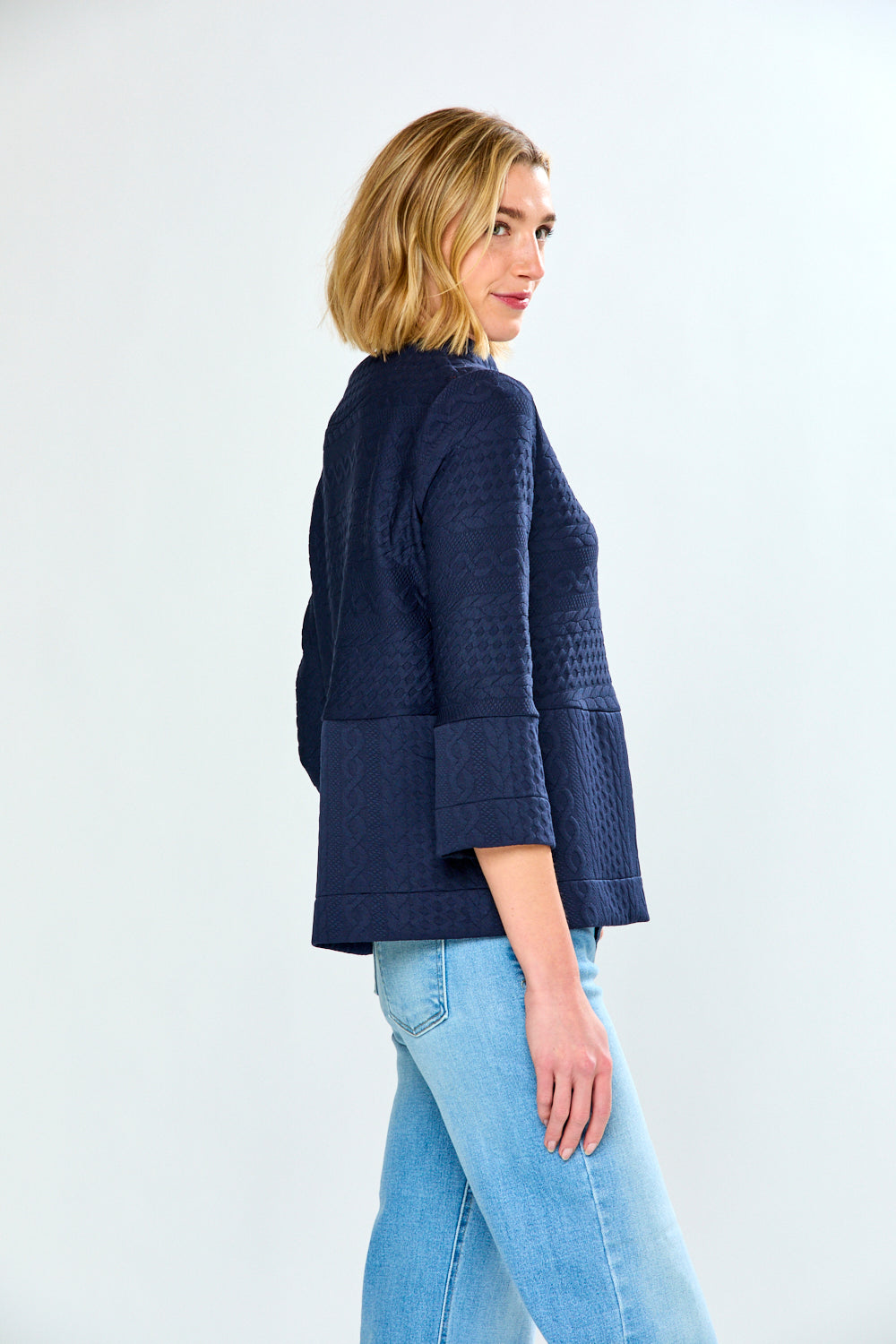 Woman wearing a blue textured jacket and light blue jeans on a white background