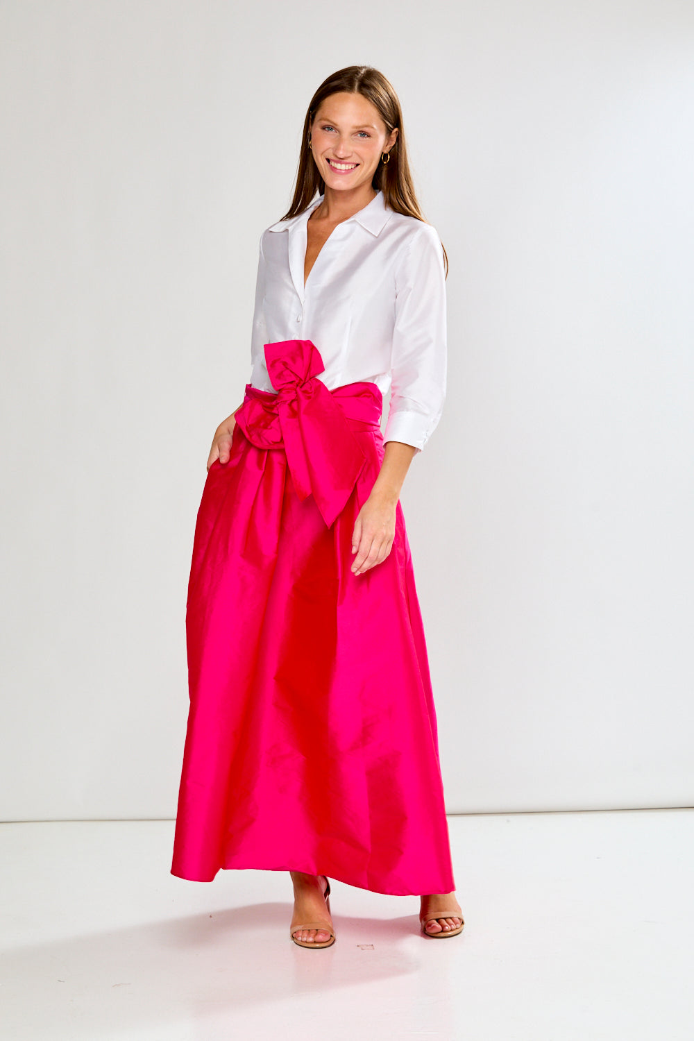 Woman wearing a white blouse and bright pink skirt on a white background