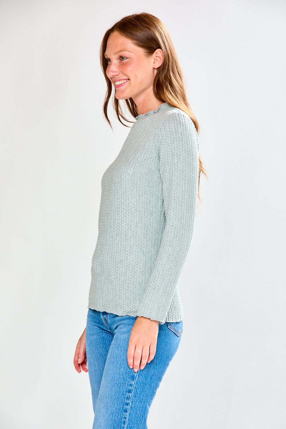 Woman wearing a light grey ribbed shirt and blue jeans on a white background