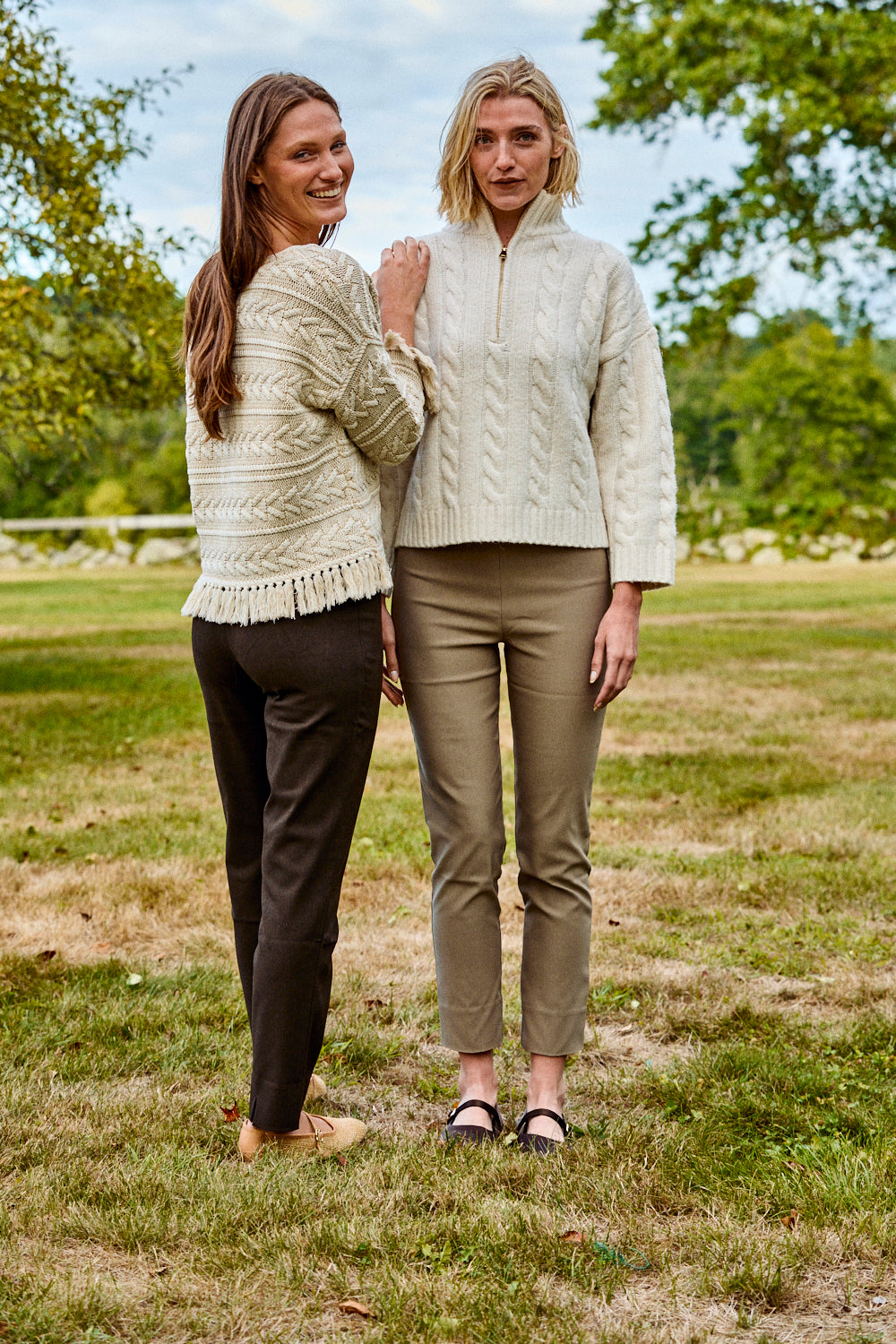 Two women standing in a grassy field wearing matching cream-colored outfits.