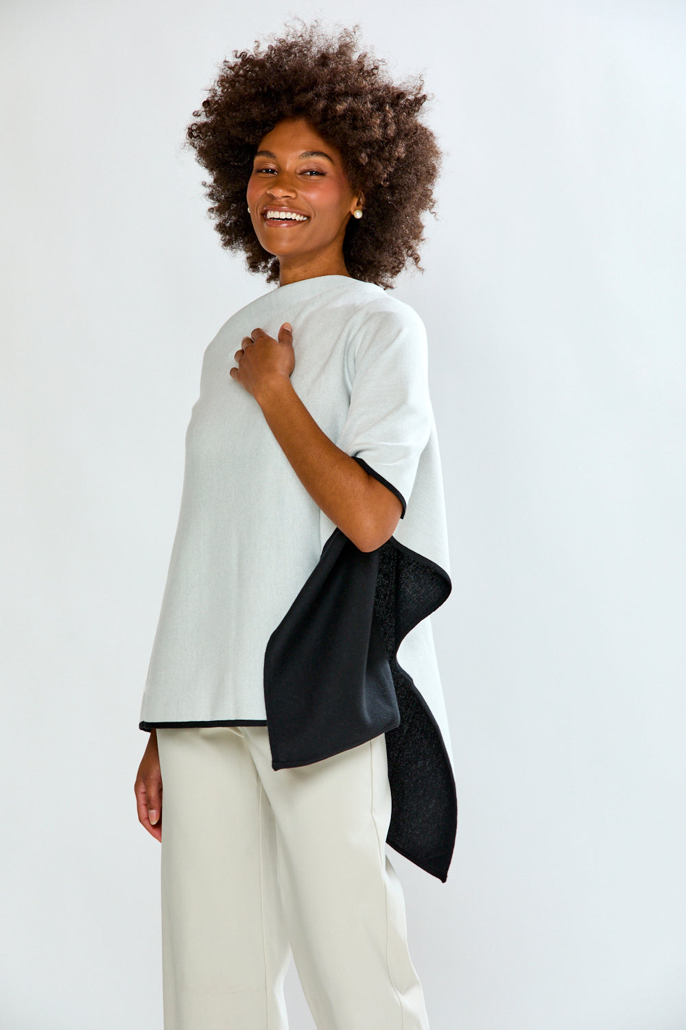 Woman wearing a white top with a black accent and white pants on a plain background