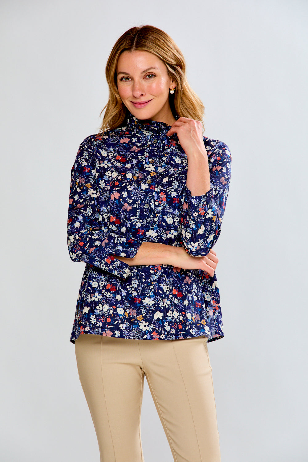 Woman wearing a floral blouse and beige pants against a plain background