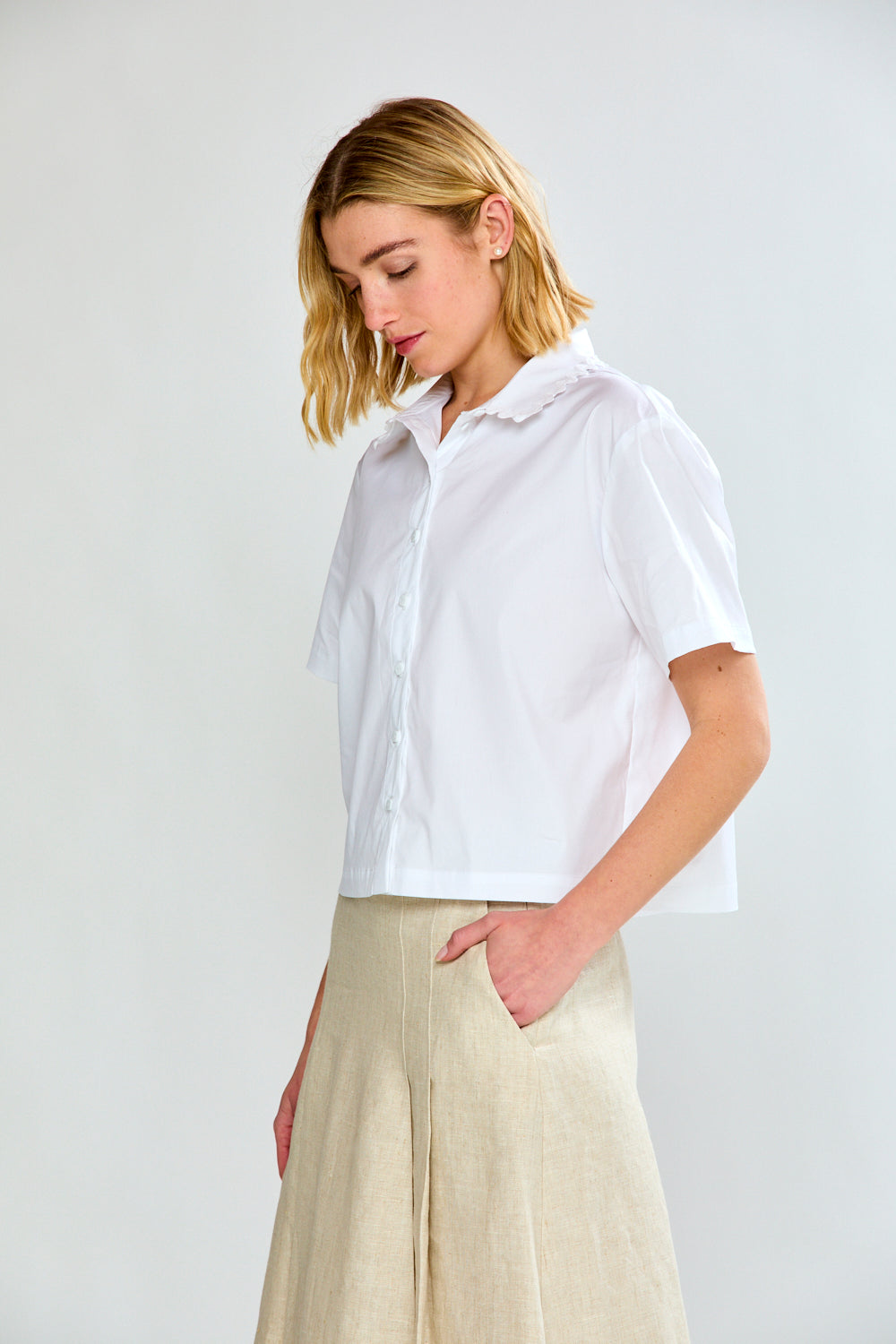 Woman wearing a white shirt and beige pants against a plain background