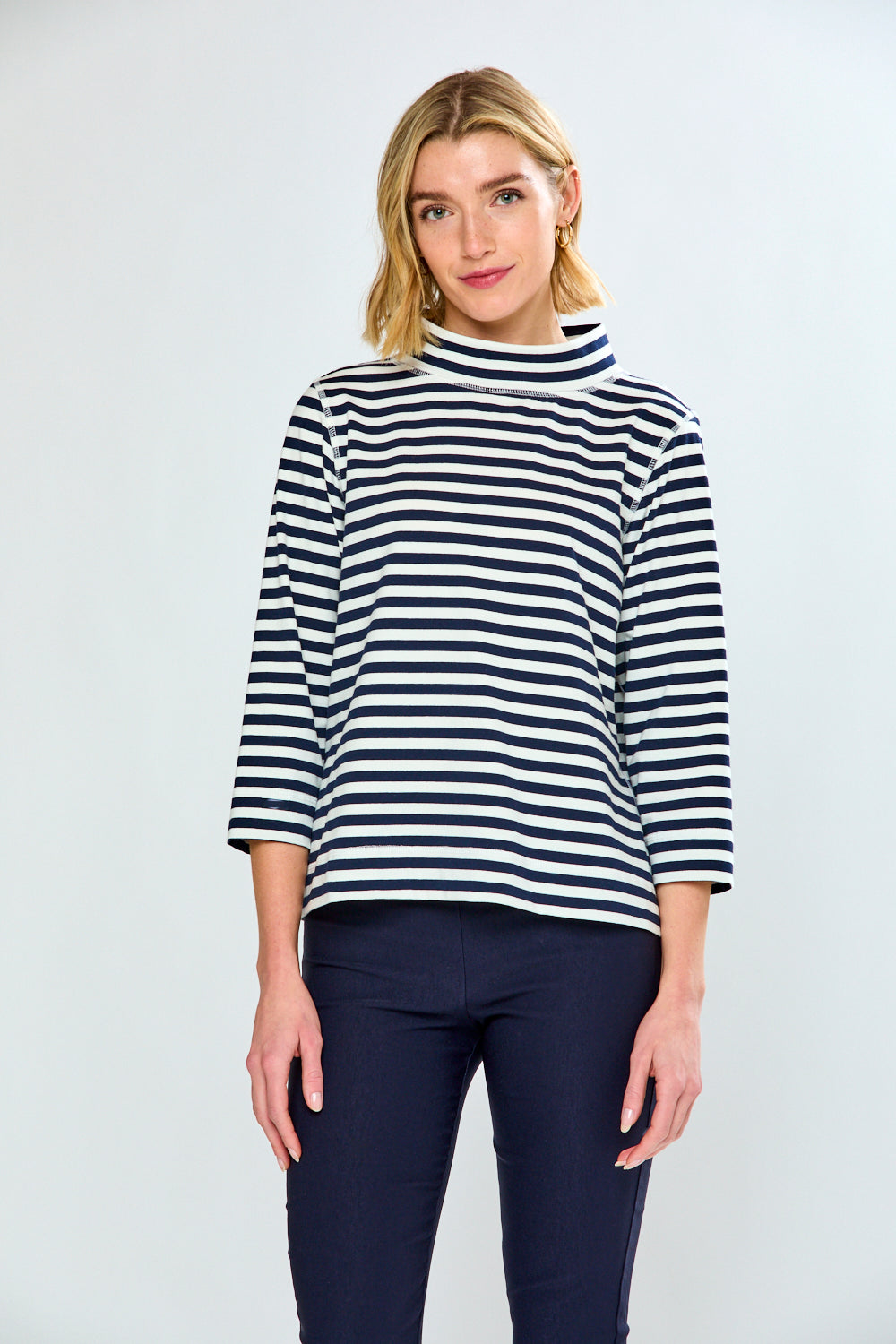 Woman wearing a black and white striped sweater with navy pants on a white background
