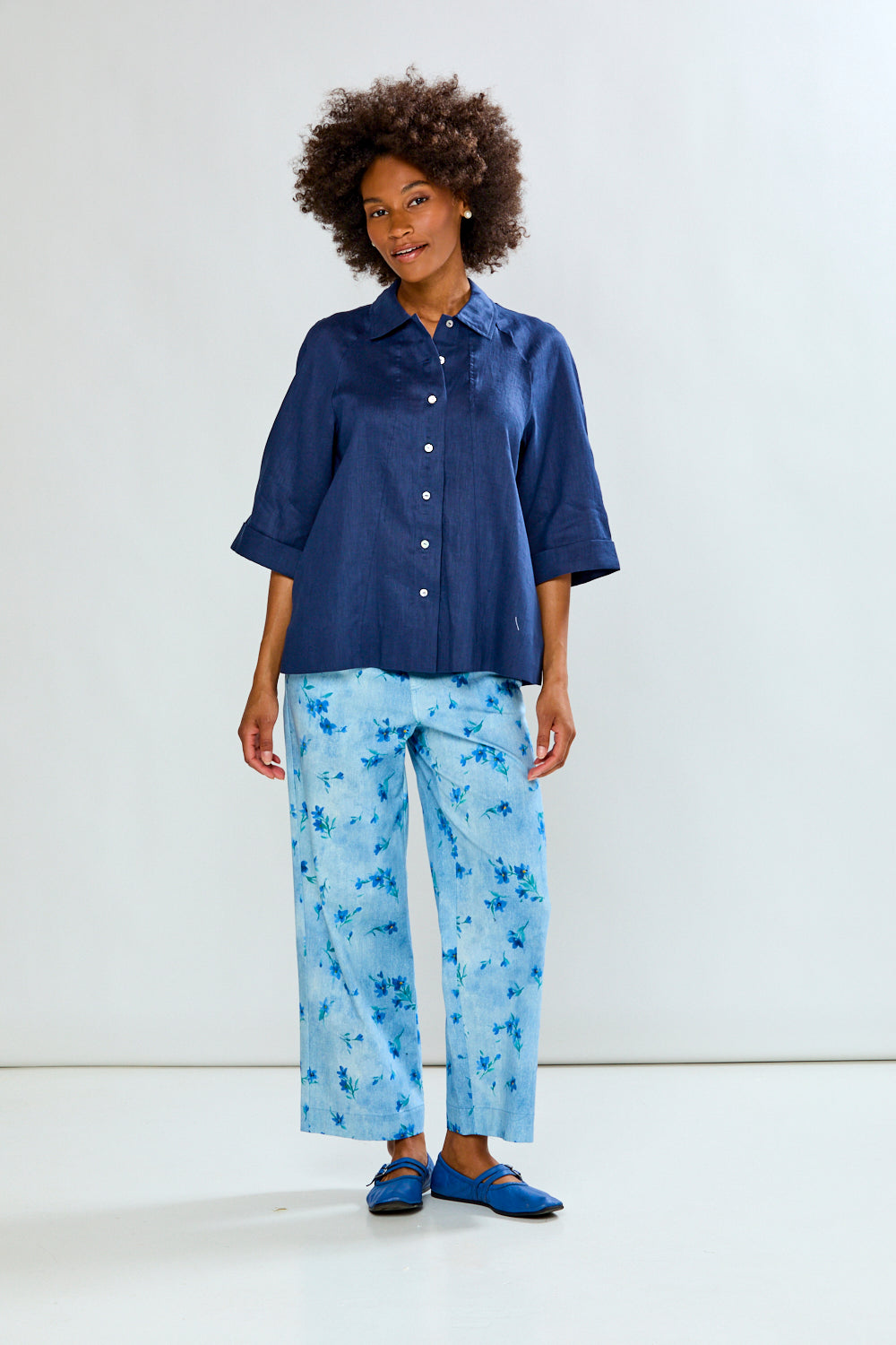 Woman wearing a blue shirt and light blue floral pants on a white background