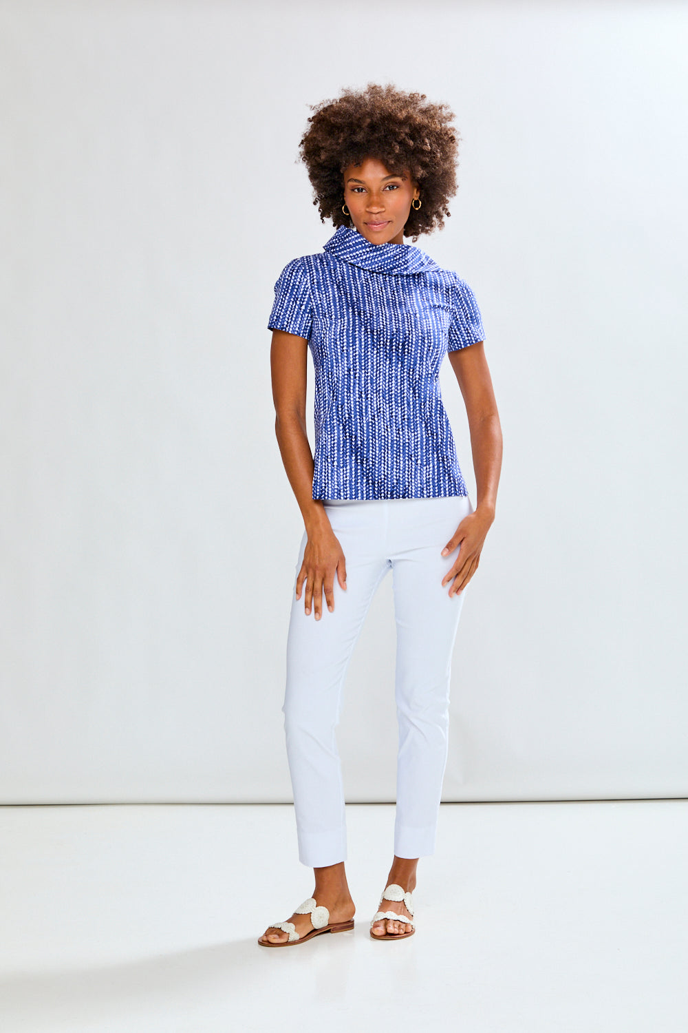Woman wearing a blue patterned top and white pants against a white background