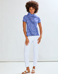 Woman wearing a blue patterned top and white pants against a white background