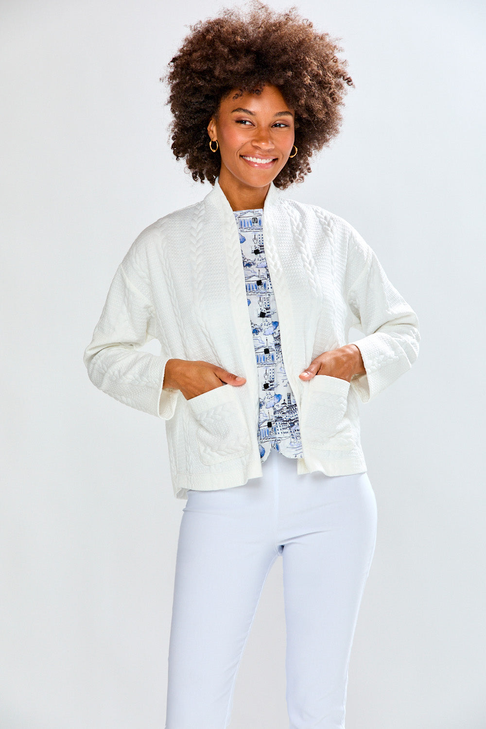 Person wearing a white cardigan and pants against a light gray background