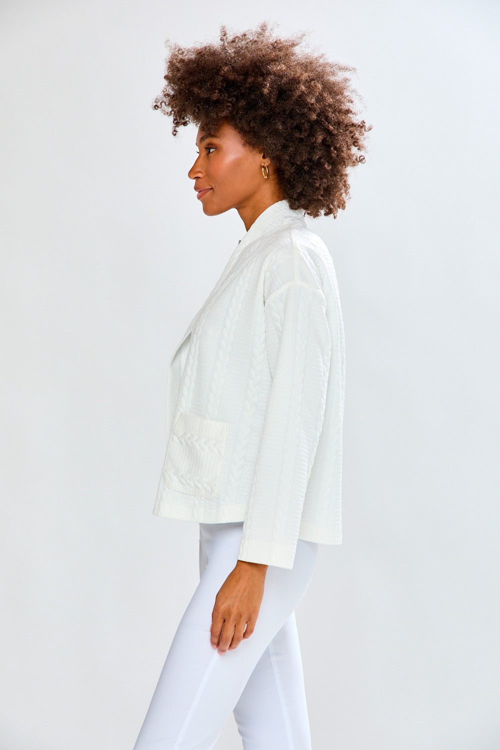 Person wearing a white cardigan and pants against a light gray background