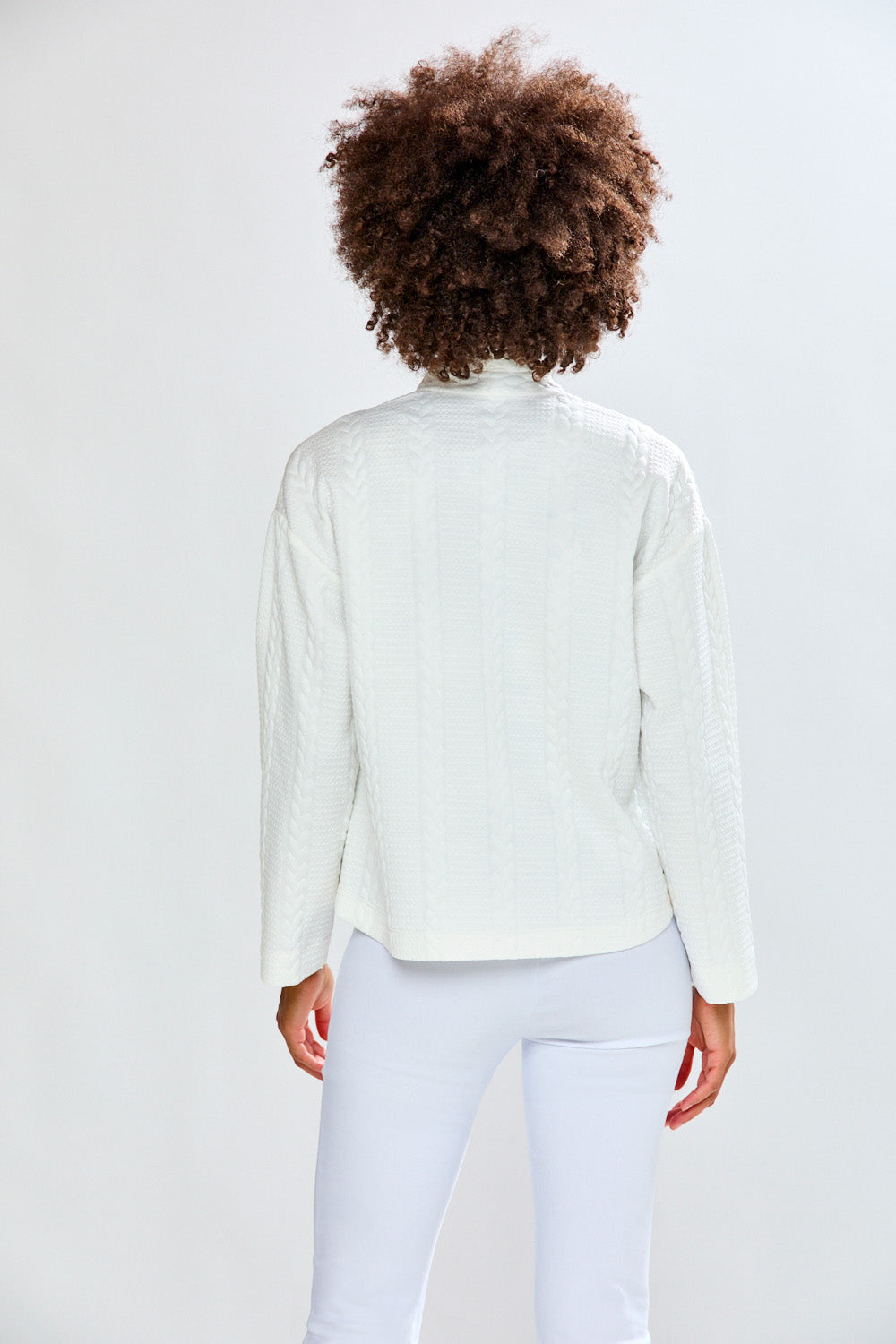 Person wearing a white cardigan and pants against a light gray background