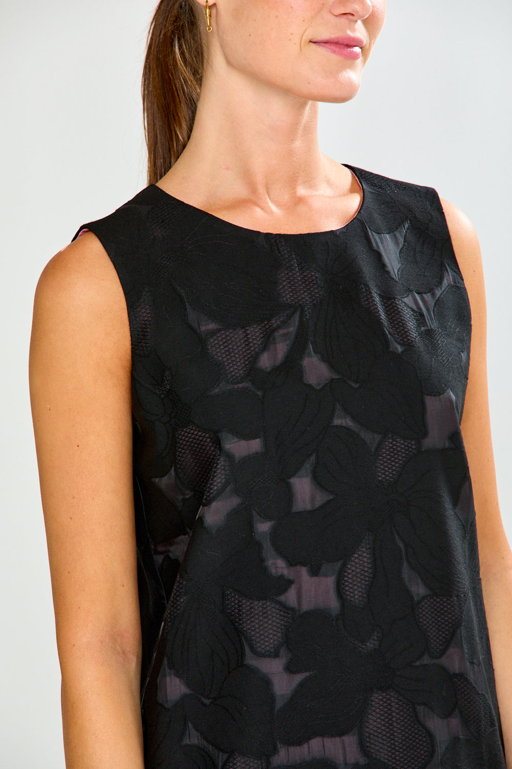 Woman wearing a black floral patterned sleeveless top against a white background