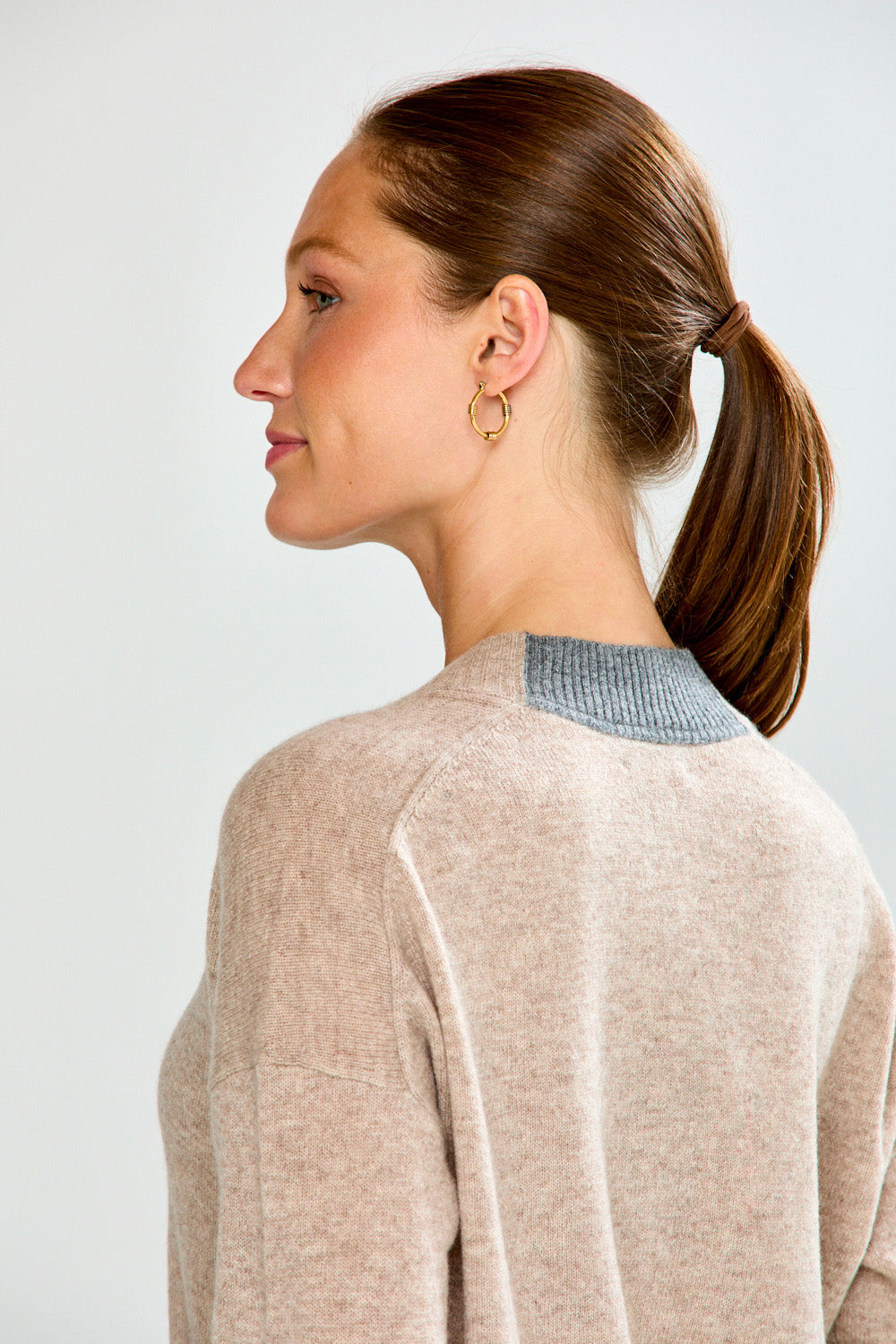 Woman wearing a beige sweater and blue jeans against a white background