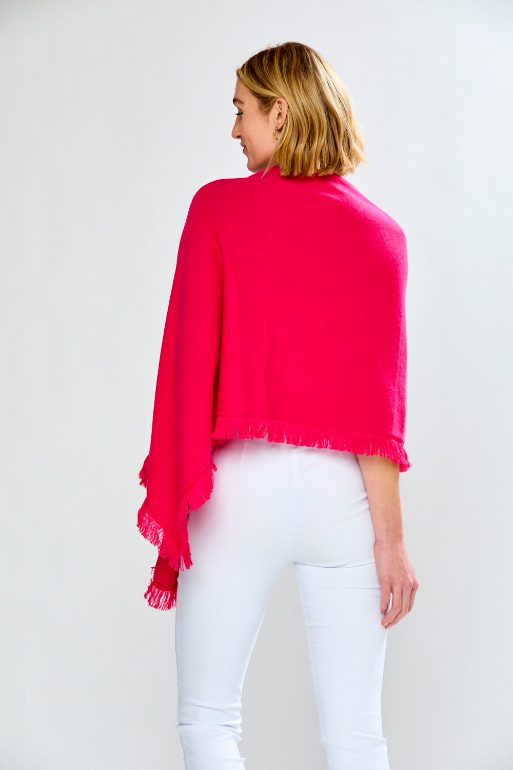 Woman wearing a bright pink shawl over a white top and pants on a plain background