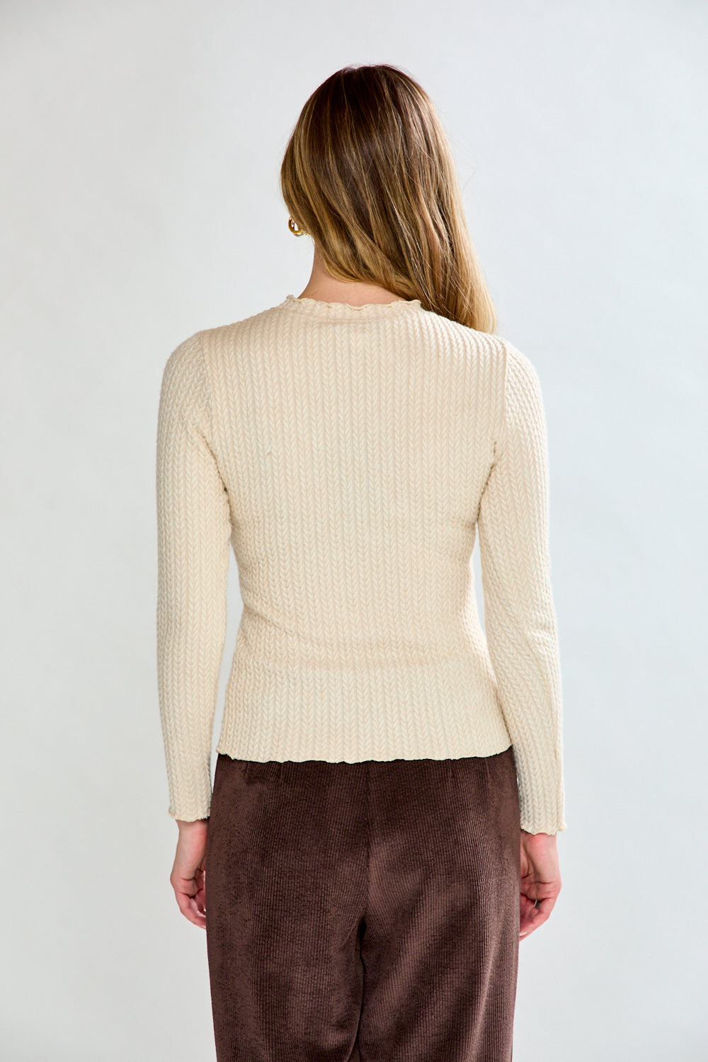 Woman wearing a beige ribbed shirt and brown pants against a white background