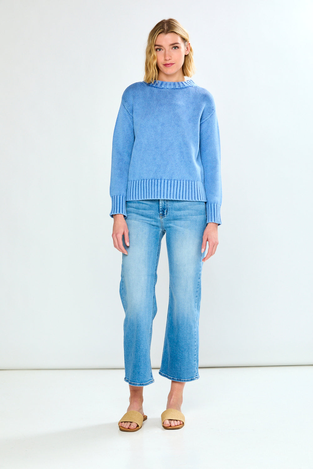 Woman wearing a blue sweater and light blue jeans on a white background