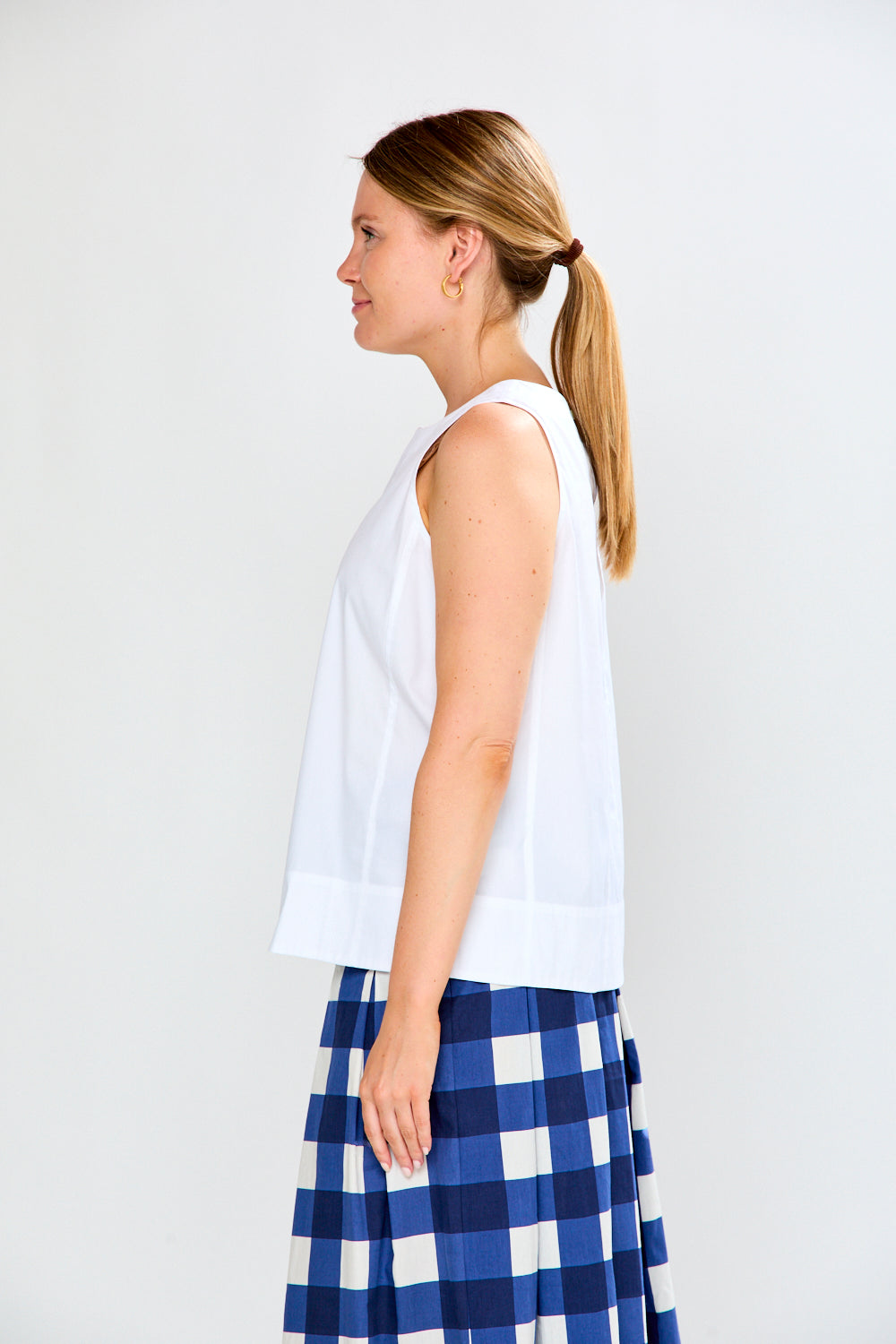 Woman wearing a white sleeveless top and blue checkered skirt on a plain background
