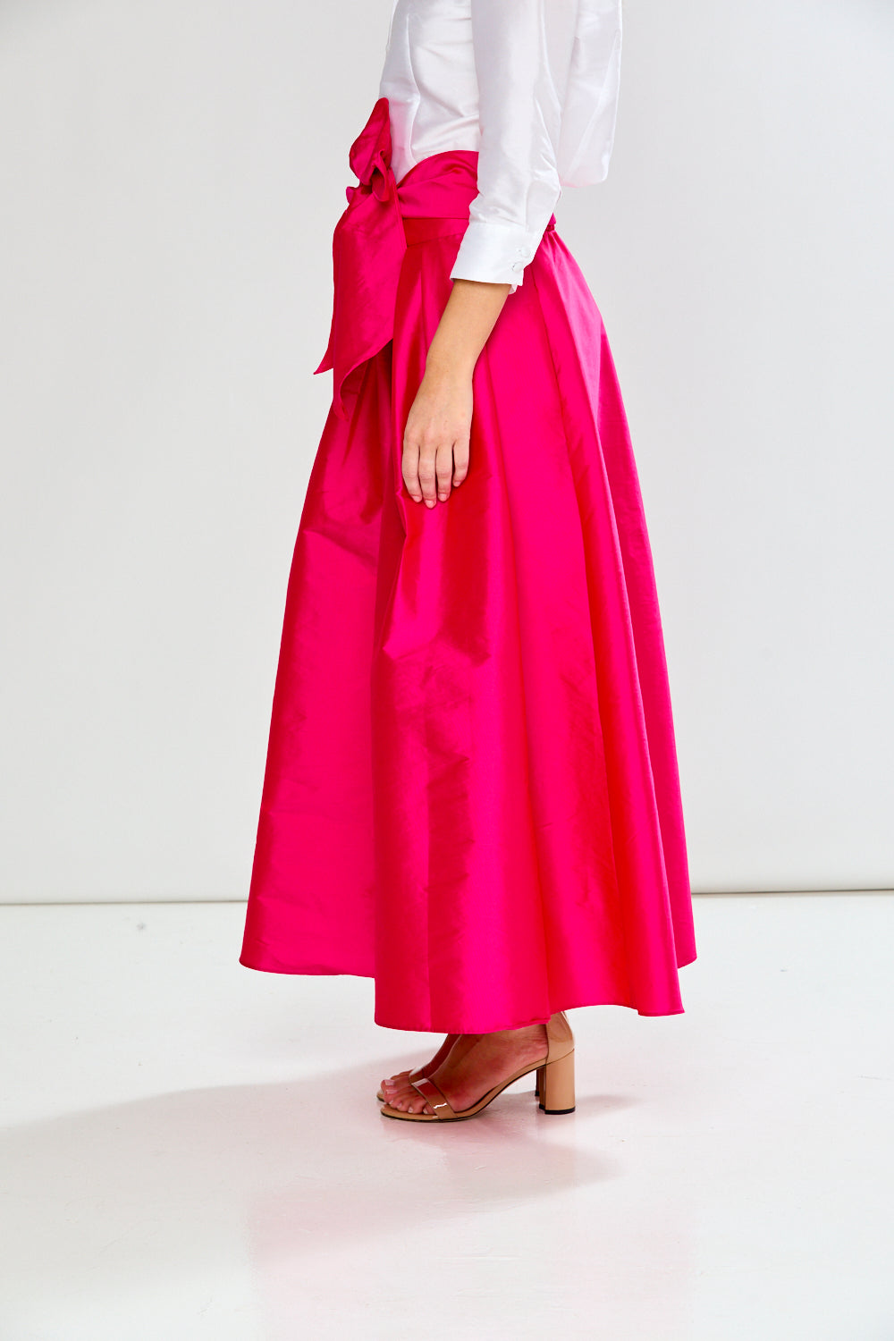 Person wearing a bright pink skirt with a white top on a light background
