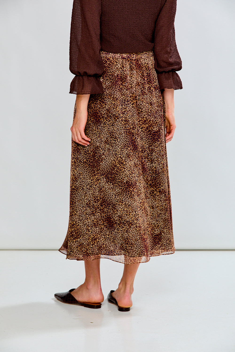 Person wearing a brown patterned skirt and brown top on a white background