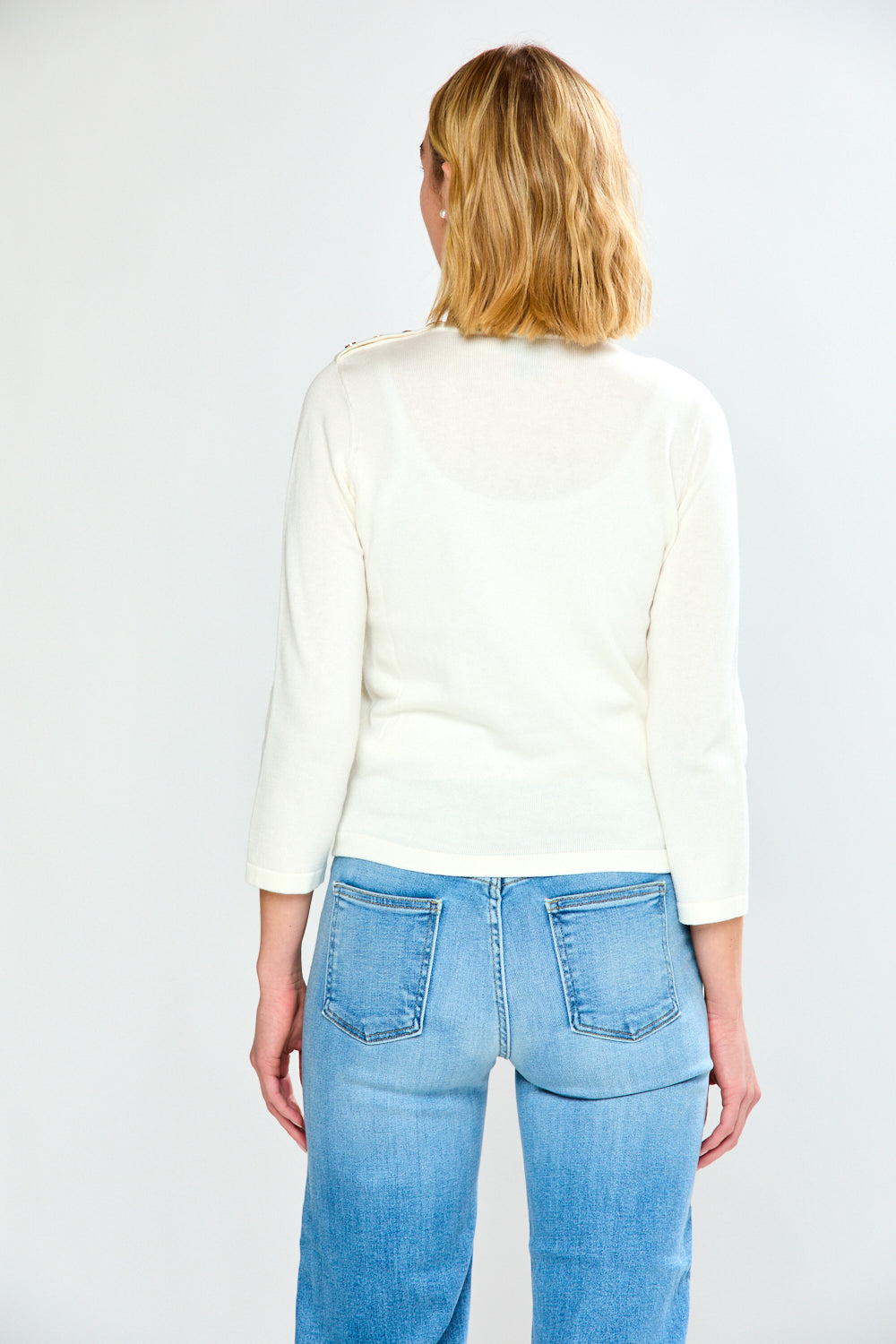 Woman wearing a white sweater and blue jeans on a plain background