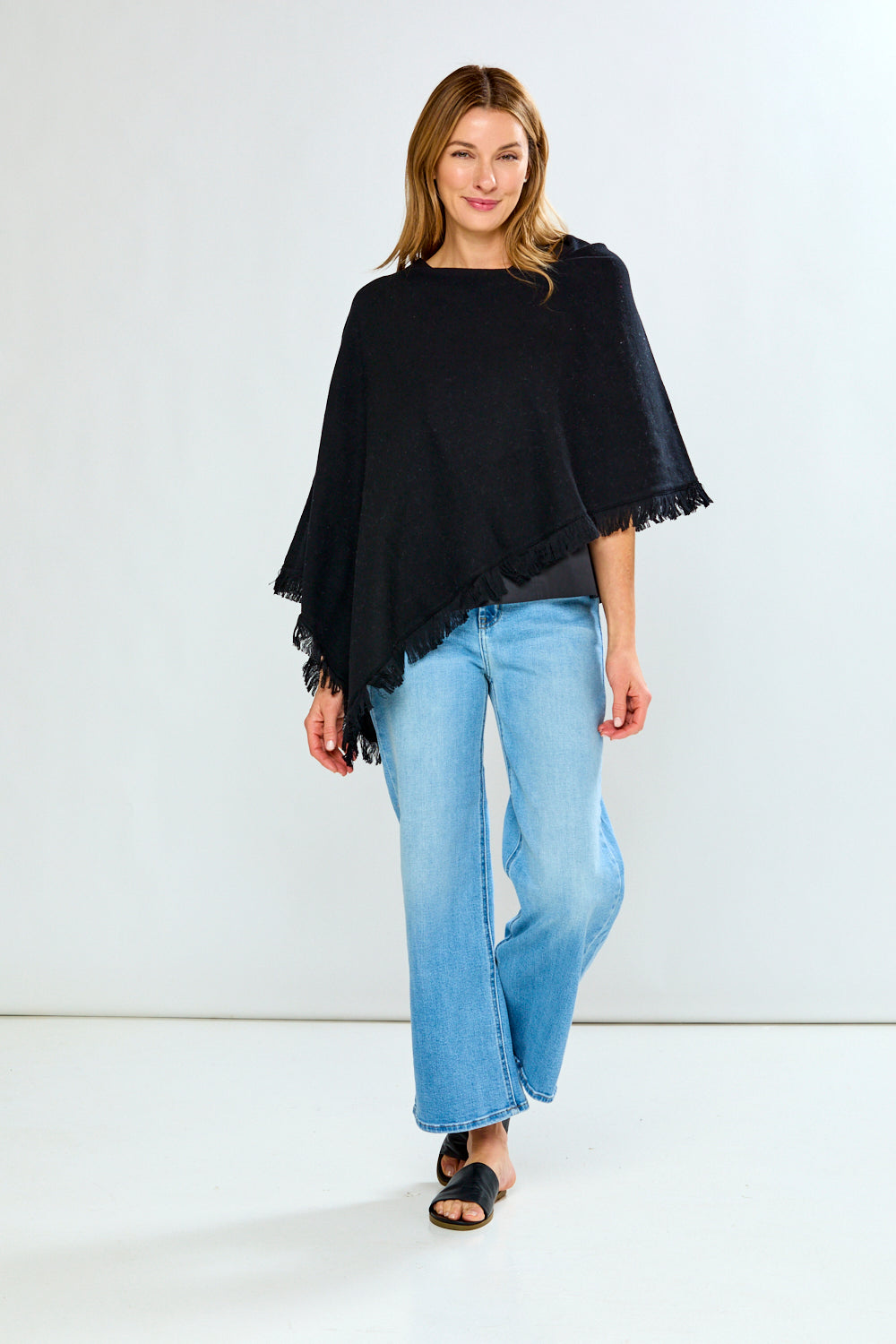 Woman wearing a black poncho and light blue jeans on a white background
