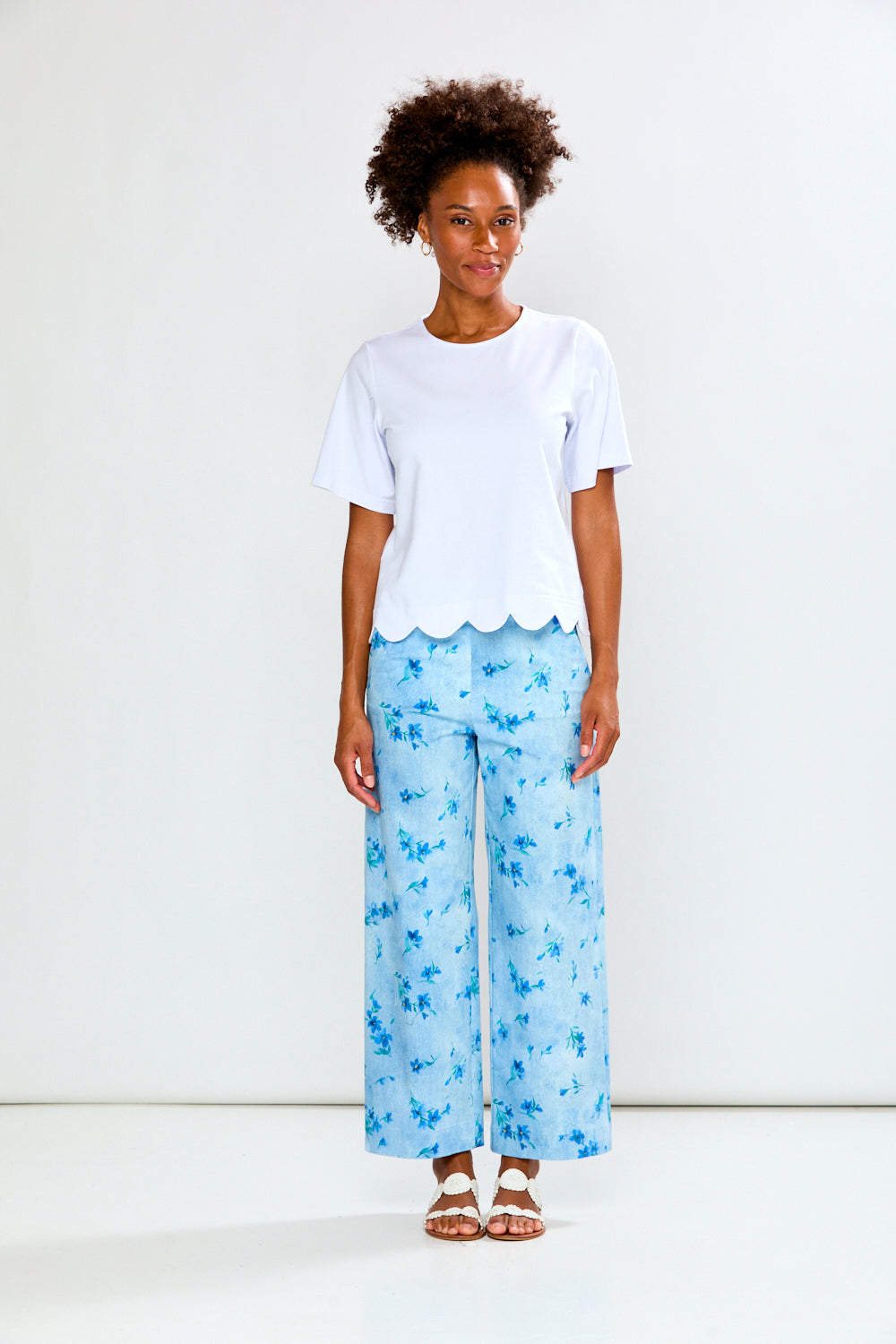 Woman wearing a white top and light blue floral pants on a white background