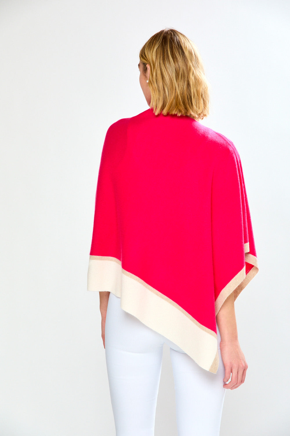Woman wearing a bright pink poncho over a white outfit on a white background
