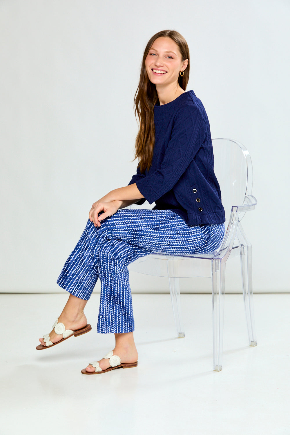 Woman wearing a navy blue cable knit top and patterned pants on a white background