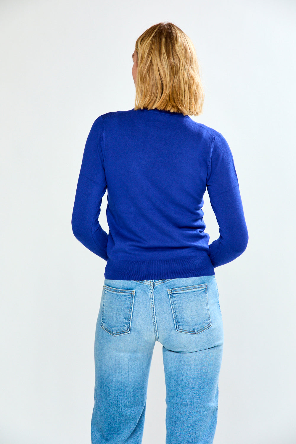 Woman wearing a blue sweater and light blue jeans on a white background