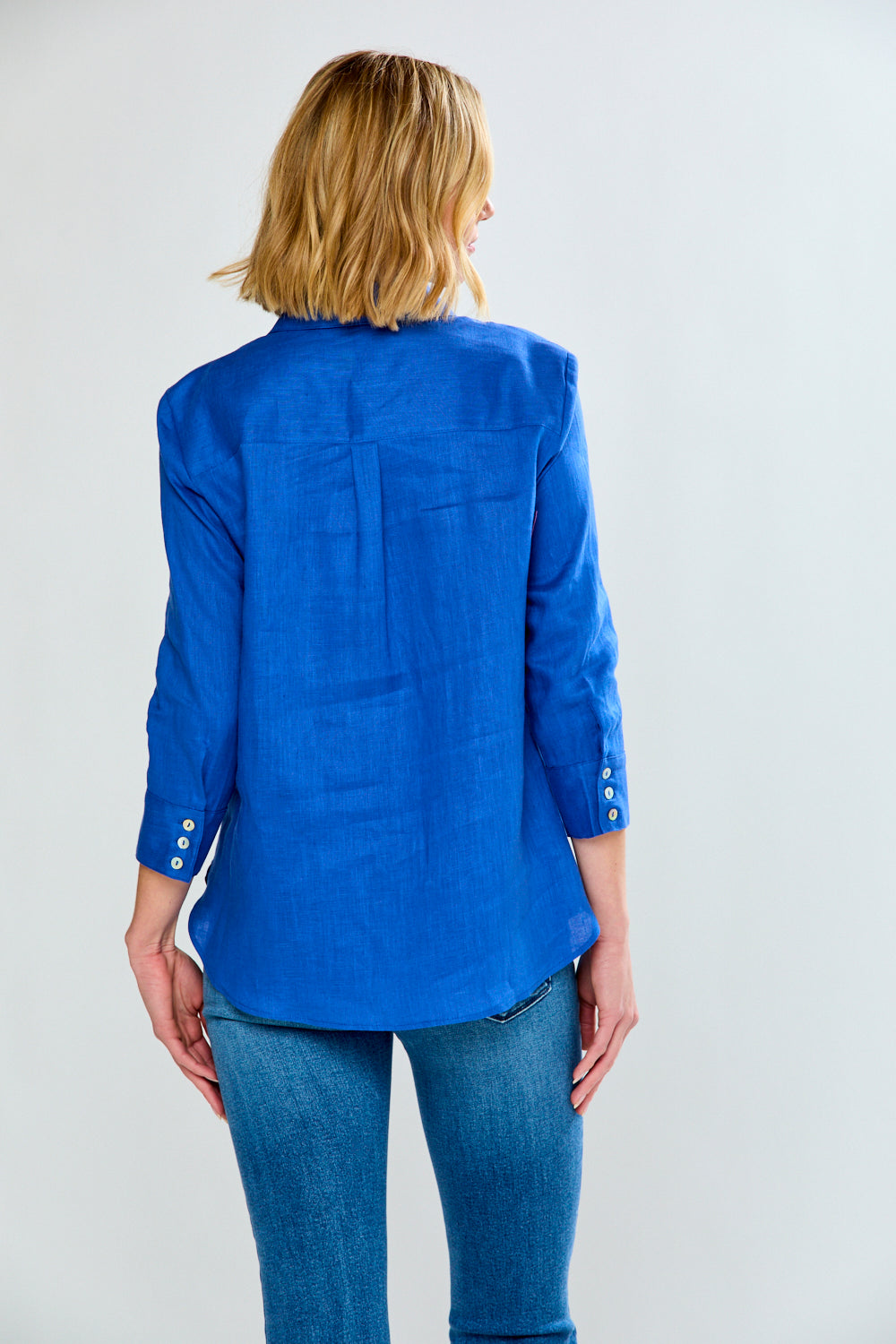 Person wearing a blue jacket and jeans on a plain background