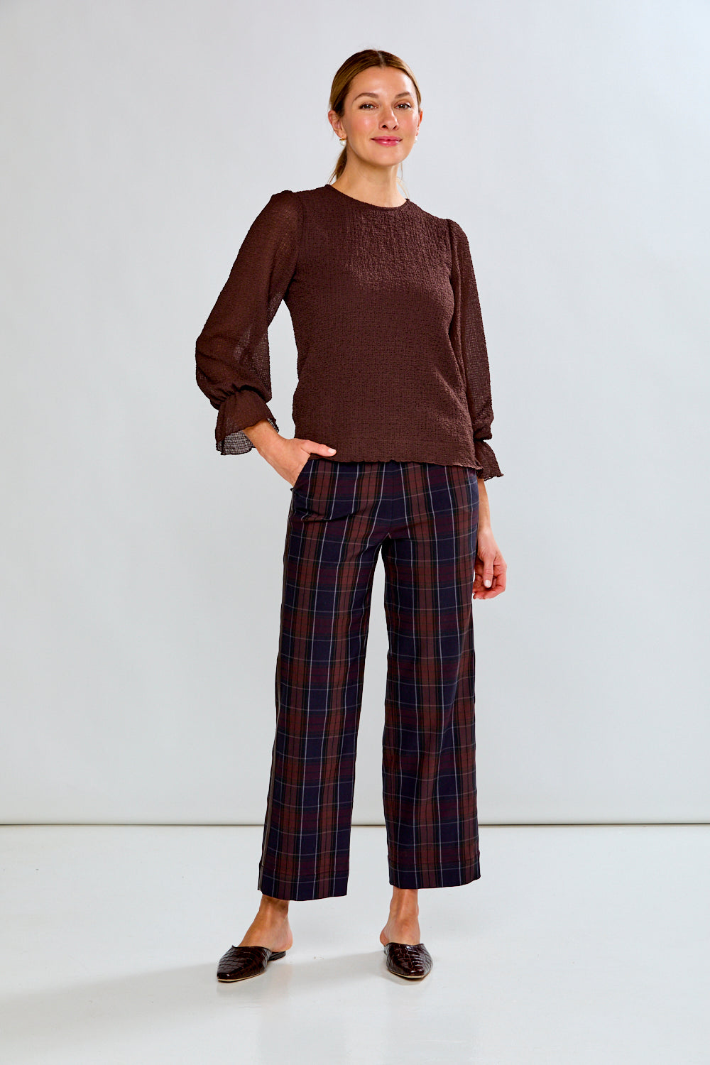 Woman wearing a brown blouse and plaid pants against a white background