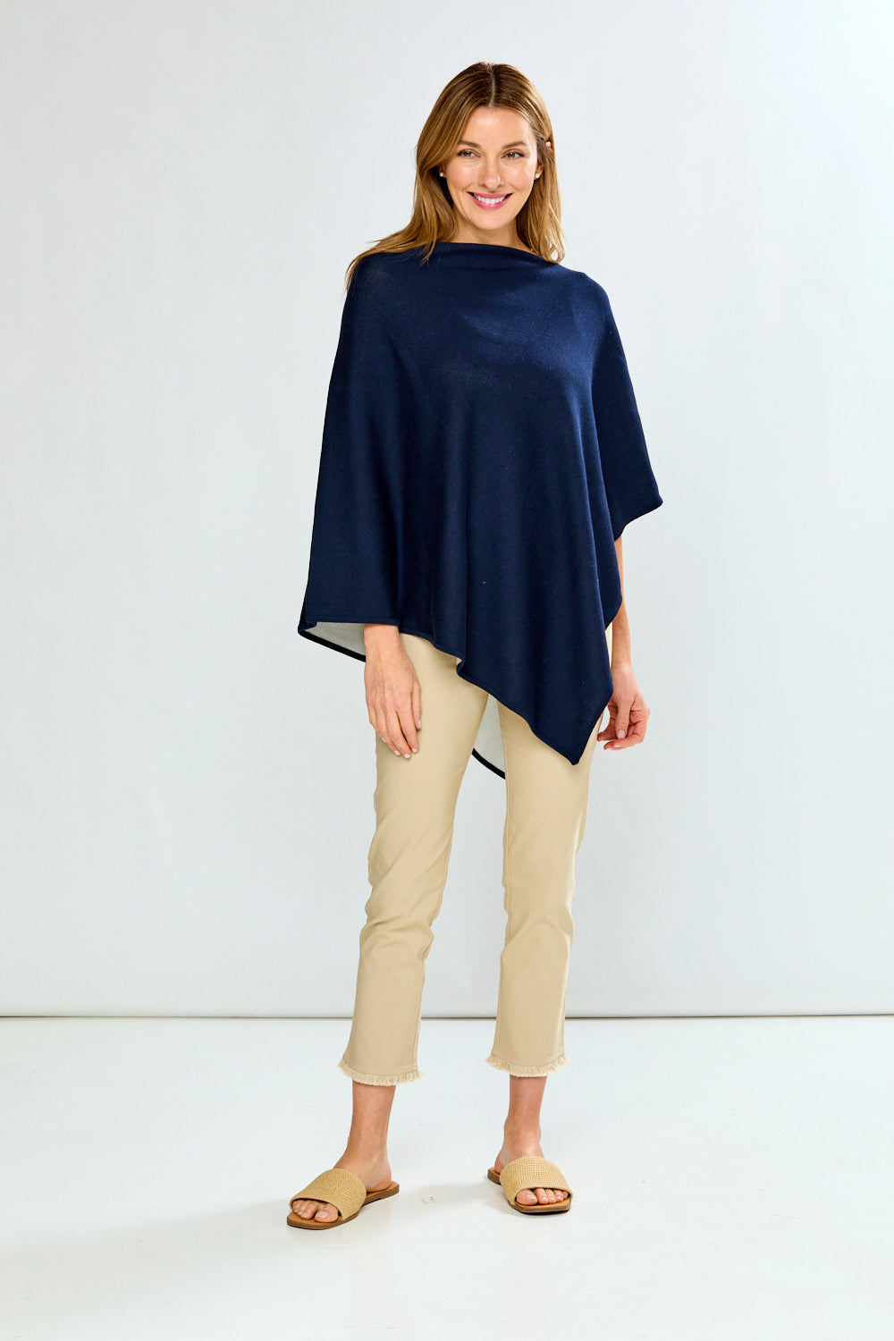 Woman wearing a navy blue poncho and beige pants on a white background