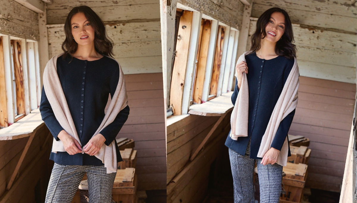 A woman stands indoors wearing a navy long-sleeve top with front buttons and a light beige shawl draped over her shoulders, paired with gray plaid pants. The photo is split into two side-by-side views in a rustic wooden room with windows.