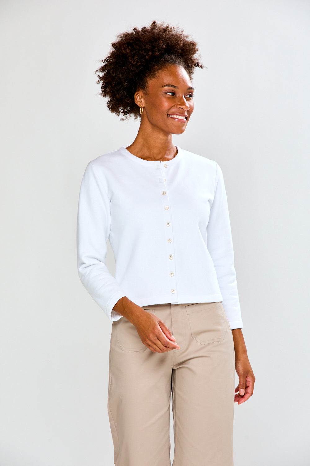 Woman wearing a white button-up shirt and beige pants against a plain background