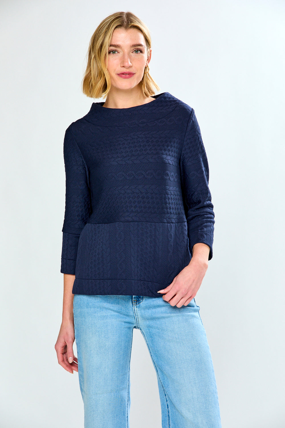 Woman wearing a navy blue textured sweater and light blue jeans on a white background
