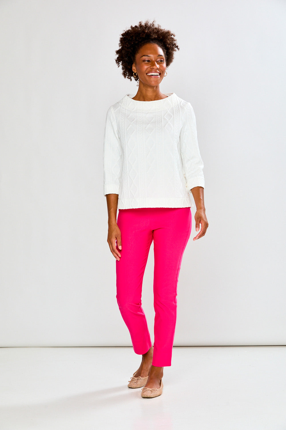 Woman wearing a white top and pink pants on a plain background