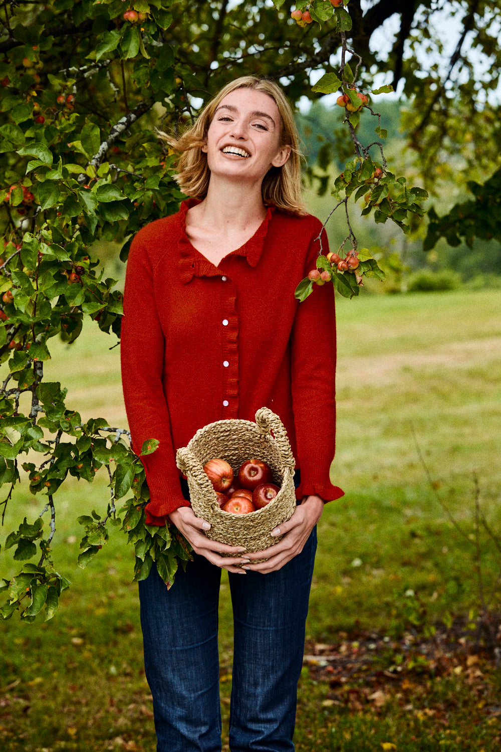 Woman in a red shirt holding a basket of apples in an orchard