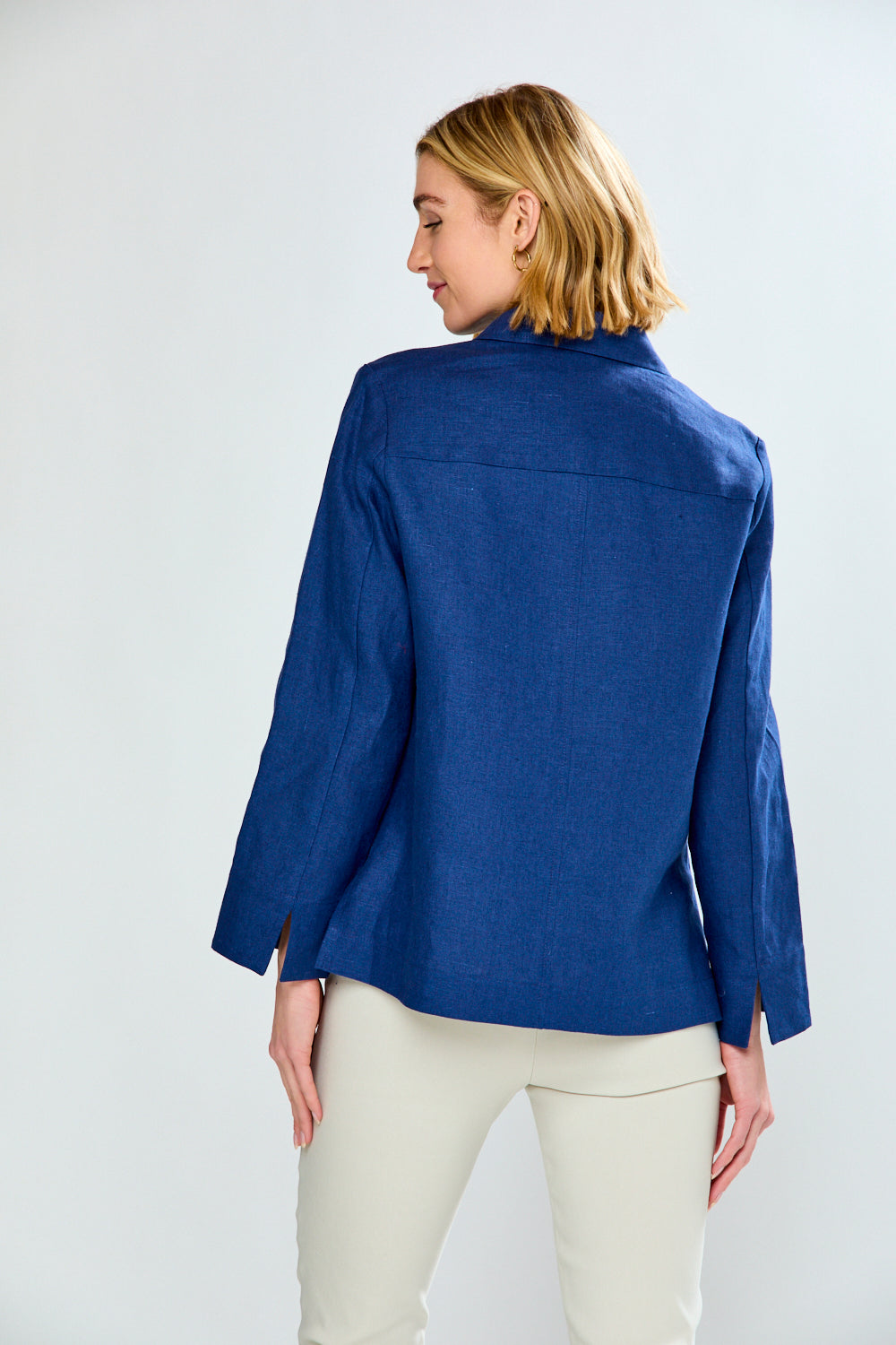 Woman wearing a blue jacket and white pants on a light gray background