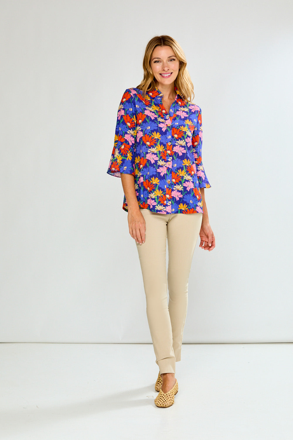 Woman wearing a colorful floral blouse and beige pants on a white background