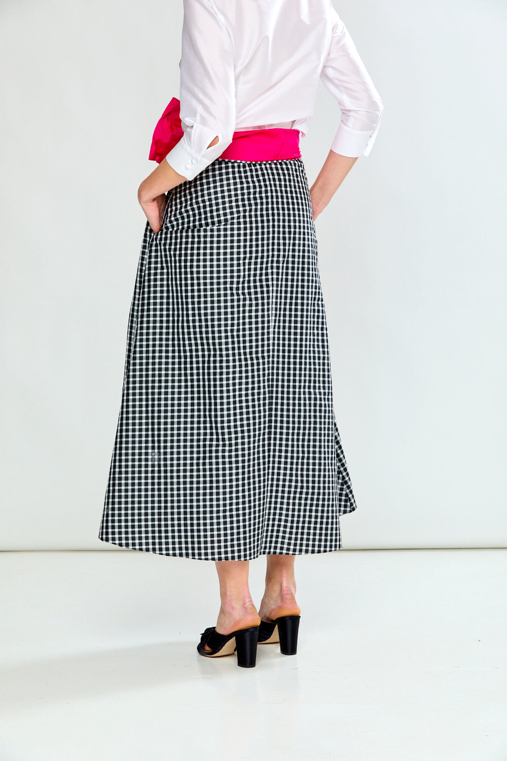 Person wearing a white blouse with a pink sweater and a black and white checkered skirt on a white background