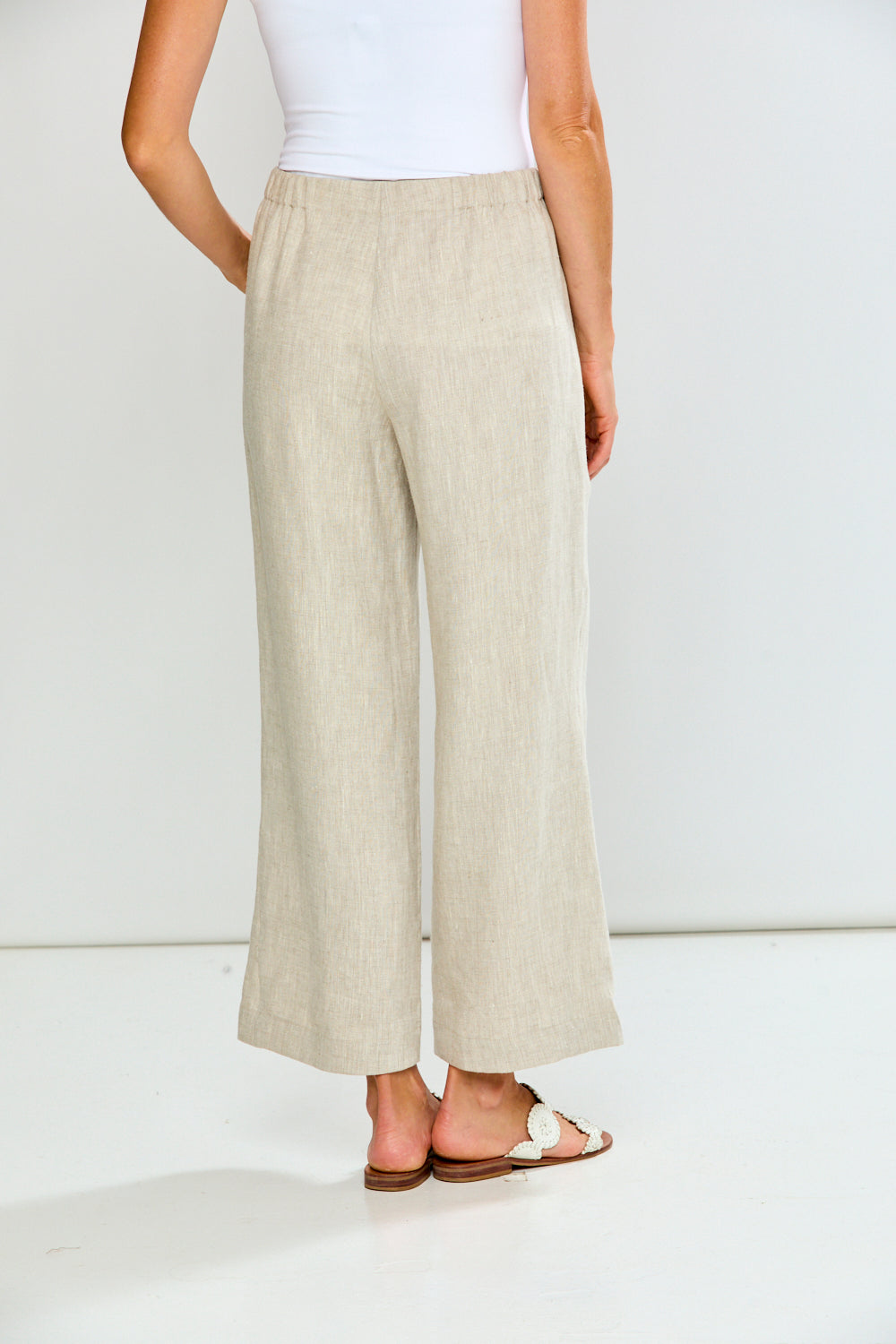 Person wearing beige wide-leg pants and a white top on a plain background