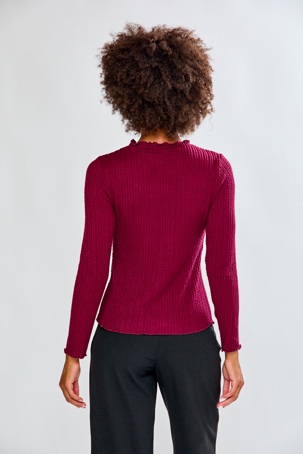 Woman wearing a burgundy shirt and black pants against a white background